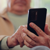 Close-up of Paul Hemens hands holding a smartphone, viewing the YourHealthNS app while seated indoors.