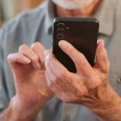 An elderly gentleman holding a phone with both hands and operating it.
