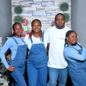 A photo of a family of four. Three are wearing blue overalls, two over blue long sleeve shirt, one is wearing a white shirt. The fourth family member has blue jeans and a white shirt.