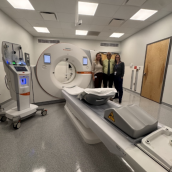 Photo of a CT scanner with 3 healthcare workers standing next to it.