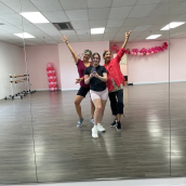 Three women in a dance studio, with arms extended, posing for a photo in front of a mirror. 