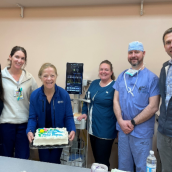 Six healthcare colleagues surround a PICC machine with a cake. 