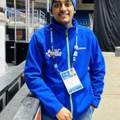A man wearing a blue hospital scrub hat, blue jacket and a lanyard with his name tag is smiling at the camera.
