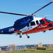 Close up image of an EHS helicopter with blue sky and buildings in the foreground.