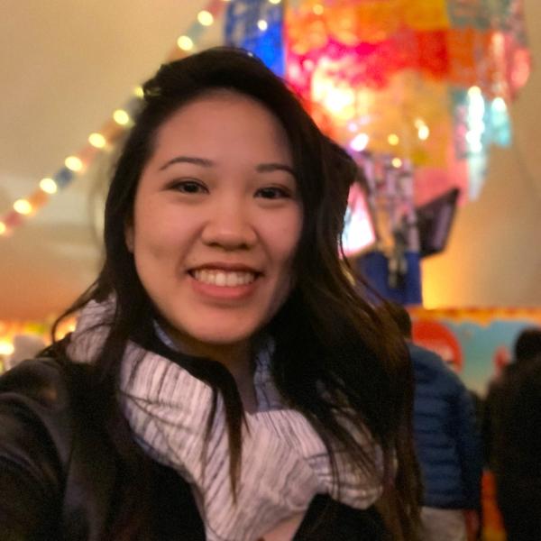 A woman of Asian descent is smiling at the camera. Colourful lights are in the background.