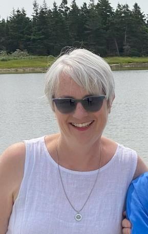 A woman wearing sunglasses is smiling in an outdoor setting.