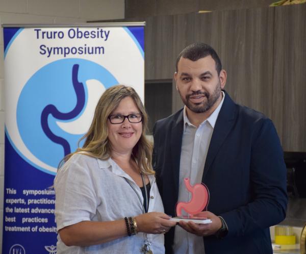 Dr. Ahmed Jad presents an award to Alana Toole, Perioperative Services Director, Northern Zone, in recognition of her commitment to advancing obesity care and improving patient accessibility. They are standing side by side, holding the award, smiling toward the camera.