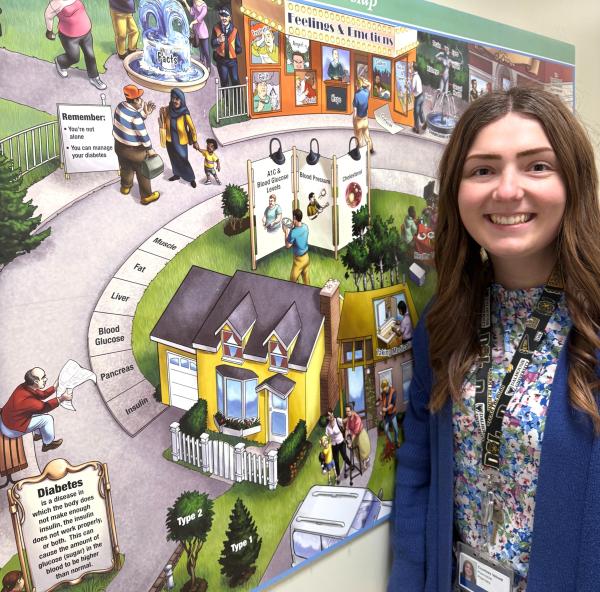 A woman standing next to an educational mural that illustrates diabetes and its effects.