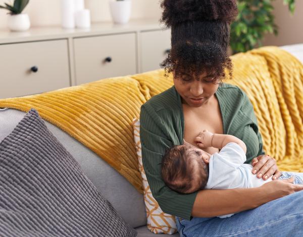 Black woman and her baby sitting on a couch. The woman is breastfeeding her baby.