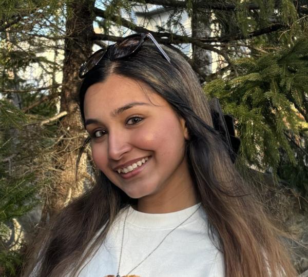 Surrounded by trees, a woman smiles at the camera in an outdoor setting.