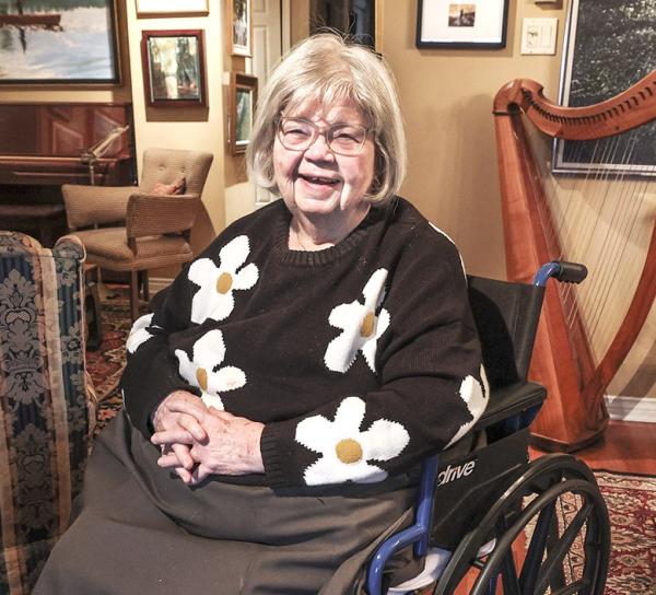 A woman sits in a wheelchair, smiling for the camera.
