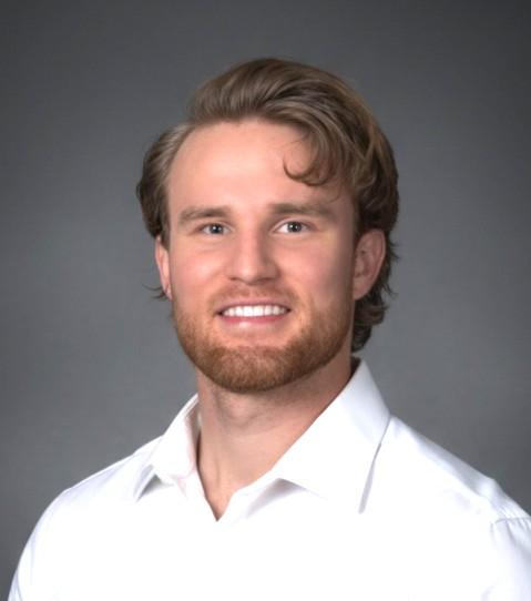 A portrait setting of a smiling man indoors wearing a white shirt with a plain wall in the background. 