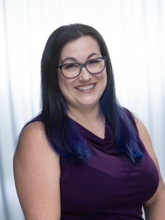 A woman wearing a purple tank top, she has black framed glasses and her hair is long black and straight with blue on the end
