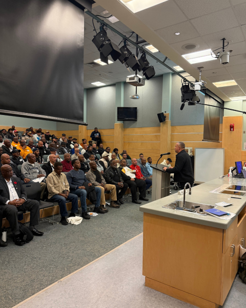 A photo of a conference for the black community. Attendees are seated and there is a speaker in front of the podium.