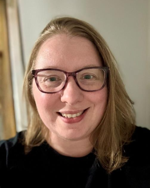 Picture of a woman with shoulder length hair smiling largely wearing glasses. 
