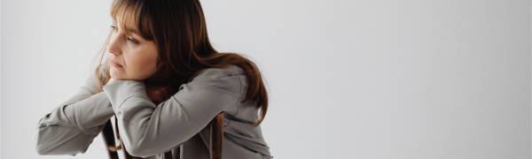 A woman sitting backwards in a chair leaning over the backrest deep in thought.
