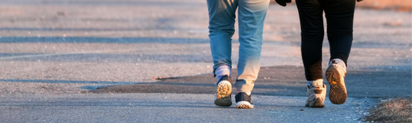 We see the legs of two people walking together down a street. We do not see their upper bodies. 