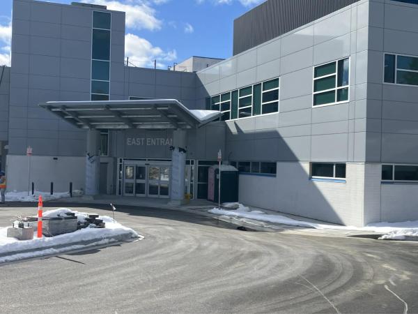 A healthcare facility viewed from outside. The building is grey and white with a large awning over the front entrance.