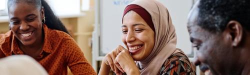 3 dark skinned people, close up image. None of them are looking at the camera but are smiling. 2 females and 1 male.