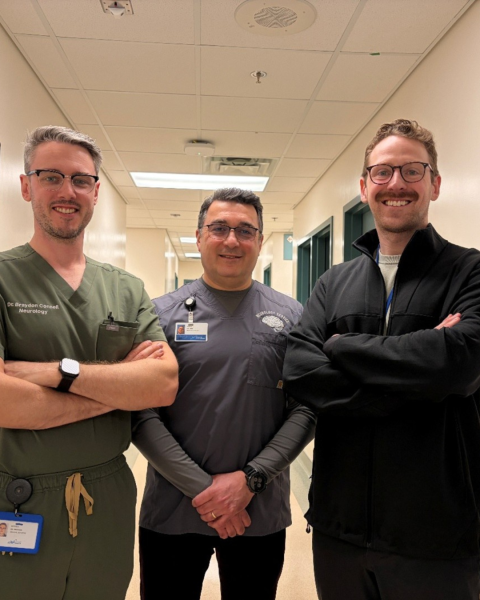 Three men stand together smiling in the hallway of a healthcare facility.