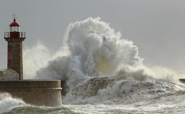 A powerful wave crashing on the rocks near a lighthouse
