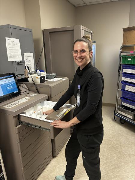A woman stands in front of a computer with equipment in a hospital room.