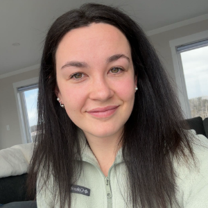 A woman with dark brown hair. She is wearing a grey sweater.