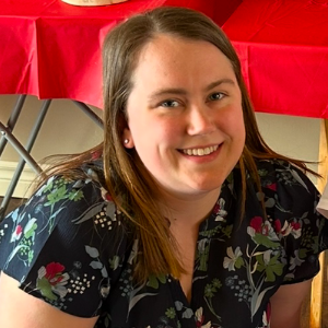 A photo of a woman with straight brown hair. She is wearing a patterned blouse.