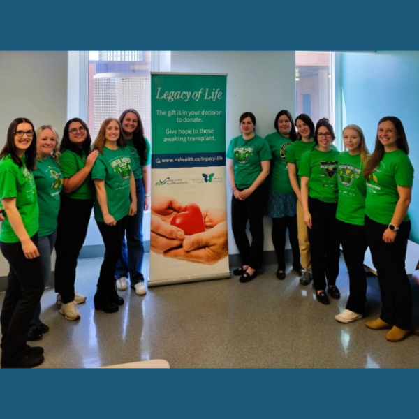 Pictured are 11 women smiling wearing green t-shirts with a 'legacy of life' stand up poster in the centre of the women. 