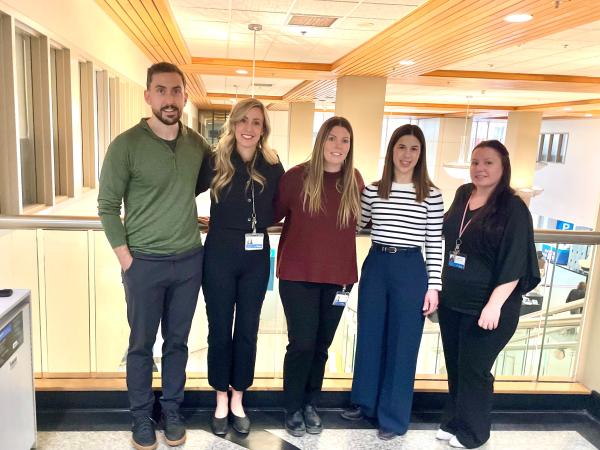 A group of five people stand together inside a health care facility smiling at the camera.