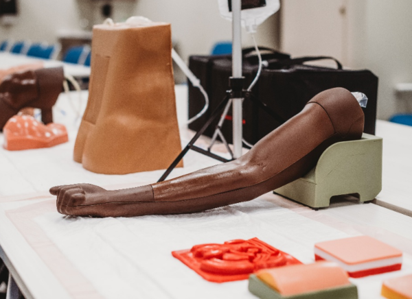 A dark skinned simulation arm is placed on a table. Other simulation body parts are on a table, but focus on the arm.