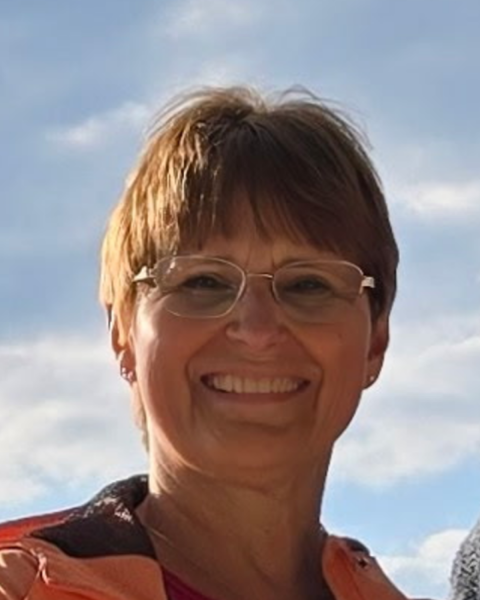 Image of a woman with short light brown hair, wearing glasses and smiling largely outside.