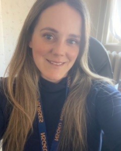 A headshot of a woman with long light brown hair smiling, wearing an NSGEU lanyard.