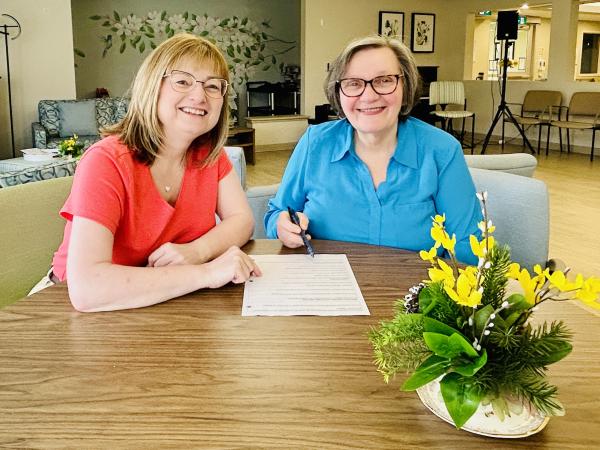 Two women sitting at a table with a paper in front of them. 