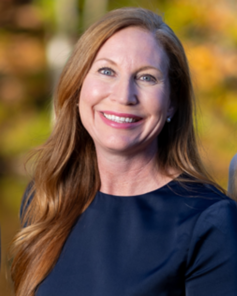 A photo of a woman with long red hair, she is wearing a navy blue blouse.