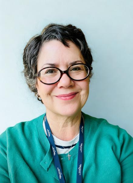 A woman with short hair and glasses wears a green shirt and is smiling at the camera.