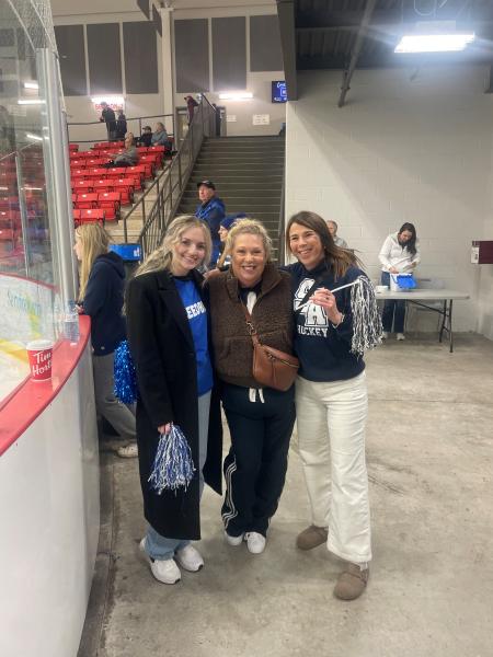3 women standing in a stadium up against the boards.