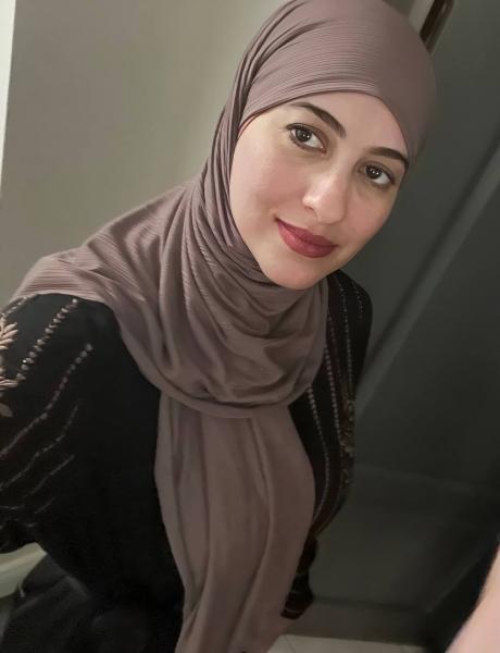 A woman with brown eyes wears is taking a selfie wearing a light brown headscarf and dark brown shirt.