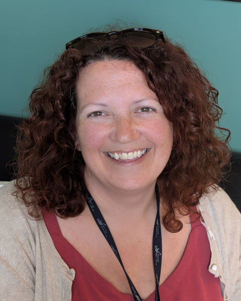 Close up image of a woman with shoulder length dark curly hair and she is smiling. 