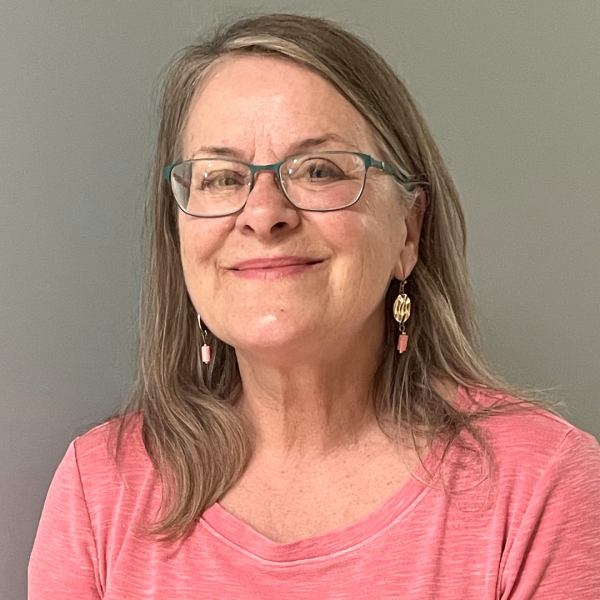 A smiling woman wearing glasses is pictured (head-and-shoulder image) against a plain background. 