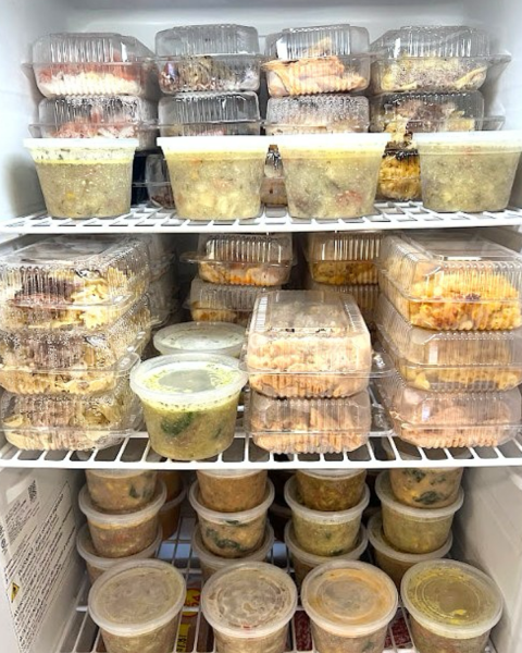 The inside of a cooling display, packed tightly with neatly stored food containers on wire shelves. 