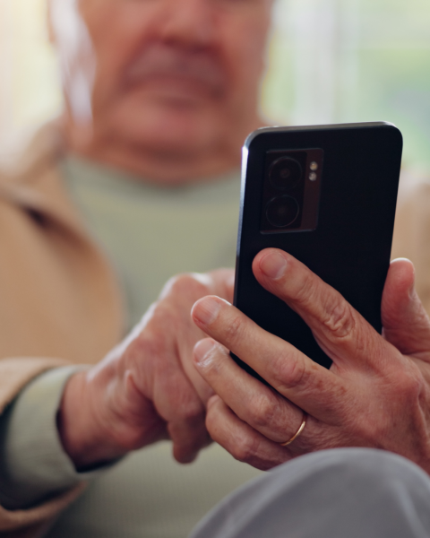 Close-up of Paul Hemens hands holding a smartphone, viewing the YourHealthNS app while seated indoors.
