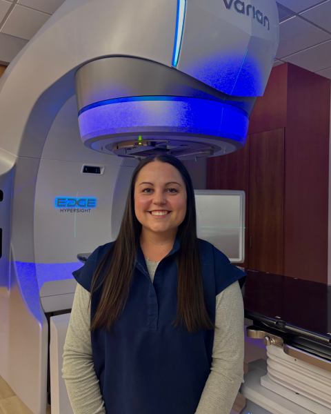 woman with long dark hair standing in front of a radiation therapy machine.