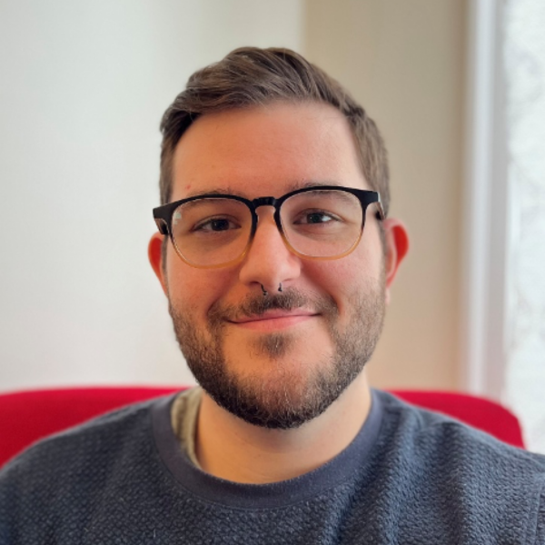 Close up image of a man with glasses and short hair. He is smiling but is not showing his teeth.