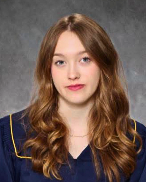 A formal portrait of a young woman in an indoor setting wearing a graduation gown looking directly at the camera. 