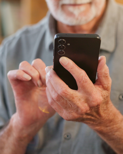 An elderly gentleman holding a phone with both hands and operating it.