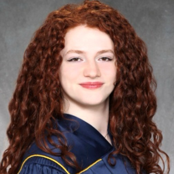 A studio-style portrait of a young woman with long curly red hair wearing a graduation gown. 