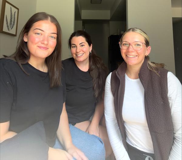 Three smiling women are seated closely together indoors. 