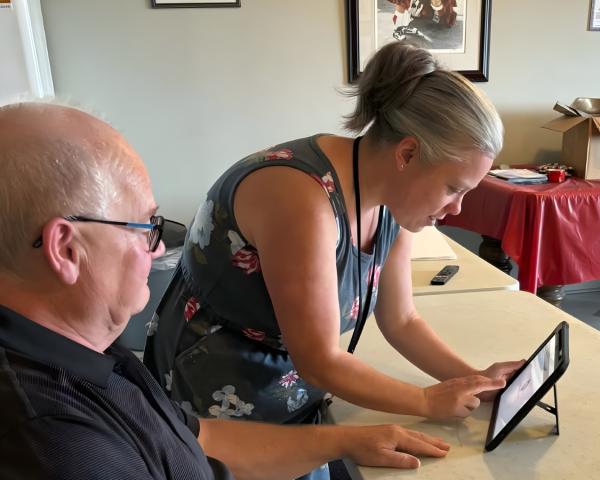 A woman with her hair in a ponytail demonstrates technology to an older person.