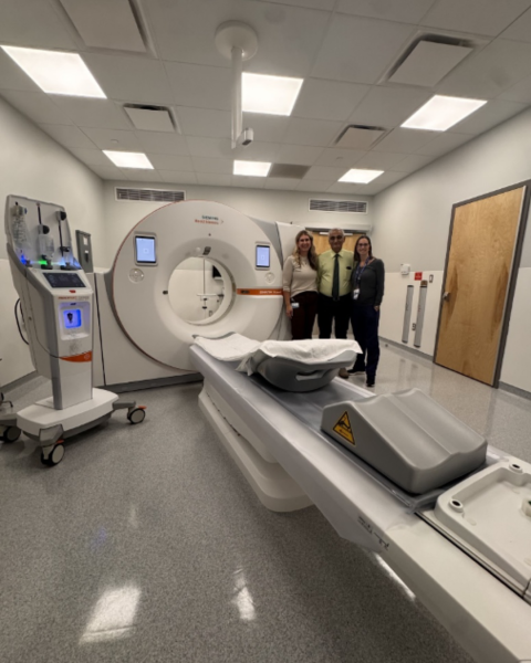 Photo of a CT scanner with 3 healthcare workers standing next to it.